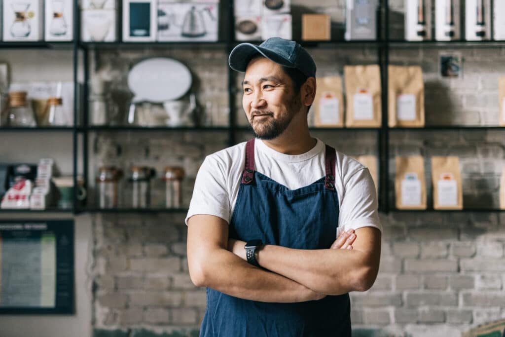 A small busienss owner of a cafe crossing his arms in front of his store